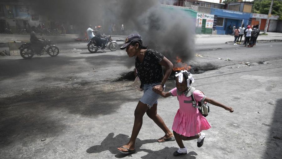 Seorang wanita berlari bersama seorang anak melewati demonstrasi menentang meningkatnya kekerasan di Port-au-Prince, Haiti, Selasa, Selasa, (29/3/2022). Protes itu bertepatan dengan peringatan 35 tahun Konstitusi Haiti 1987. (AP Photo/Odelyn Joseph)