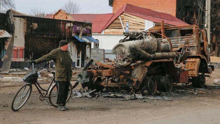 Seorang penduduk setempat berdiri di samping kendaraan militer Rusia yang hancur, saat serangan Rusia ke Ukraina berlanjut di kota Trostianets, di wilayah Sumy, Ukraina, Senin (28/3/2022). (REUTERS/Oleg Pereverzev)