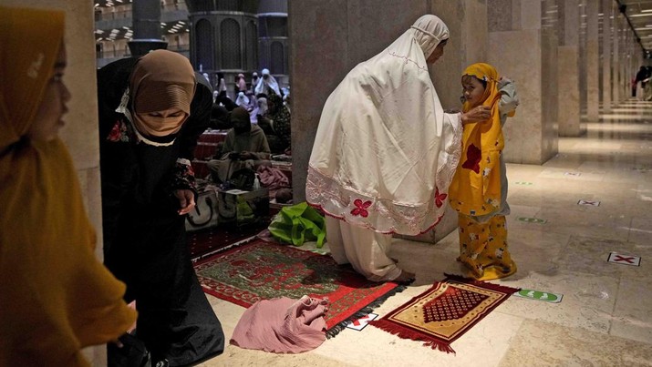 A woman helps her daughter to put on a praying robe prior to the start of 'tarawih' an evening prayer marking the first eve of the holy fasting month of Ramadan at Istiqlal Mosque in Jakarta, Indonesia, Saturday, April 2, 2022. (AP Photo/Dita Alangkara)