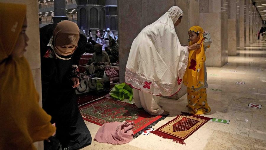 A woman helps her daughter to put on a praying robe prior to the start of 'tarawih' an evening prayer marking the first eve of the holy fasting month of Ramadan at Istiqlal Mosque in Jakarta, Indonesia, Saturday, April 2, 2022. (AP Photo/Dita Alangkara)