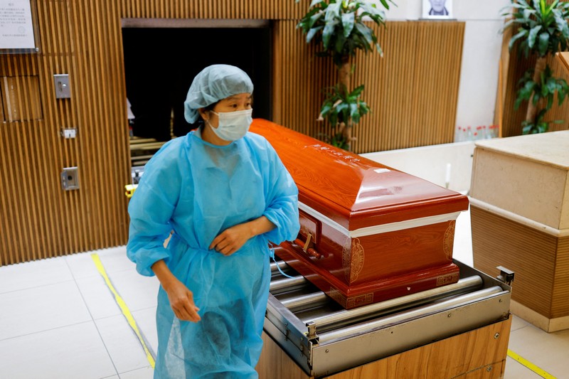 Petugas memindahkan  jenazah ke dalam kontainer berpendingin ksaat kamar jenazah kehabisan ruang di tengah wabah penyakit coronavirus (COVID-19) di luar rumah duka di Hong Kong,  Sabtu (5/3/2022). (REUTERS/Tyrone Siu)