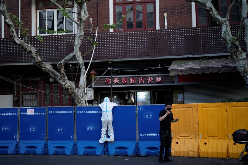 Seseorang dengan pakaian pelindung meemanjat barikade yang dipasang di sekitar area tertutup, selama penguncian untuk mengekang penyebaran penyakit coronavirus (COVID-19) di Shanghai, China, Senin (11/4/2022). (REUTERS/Aly Song)