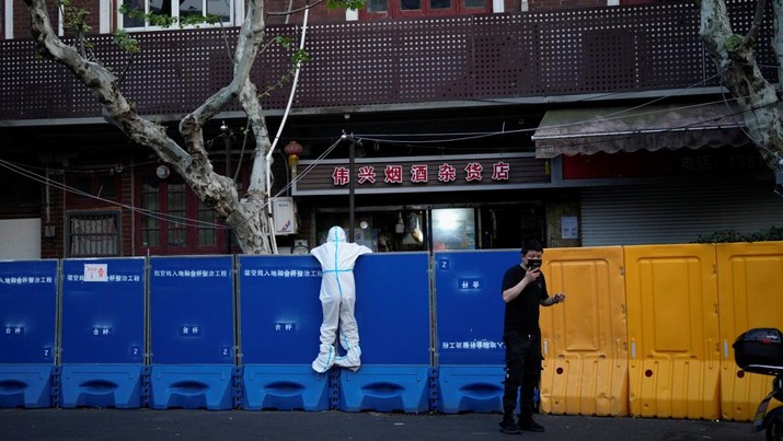 Seseorang dengan pakaian pelindung meemanjat barikade yang dipasang di sekitar area tertutup, selama penguncian untuk mengekang penyebaran penyakit coronavirus (COVID-19) di Shanghai, China, Senin (11/4/2022). (REUTERS/Aly Song)