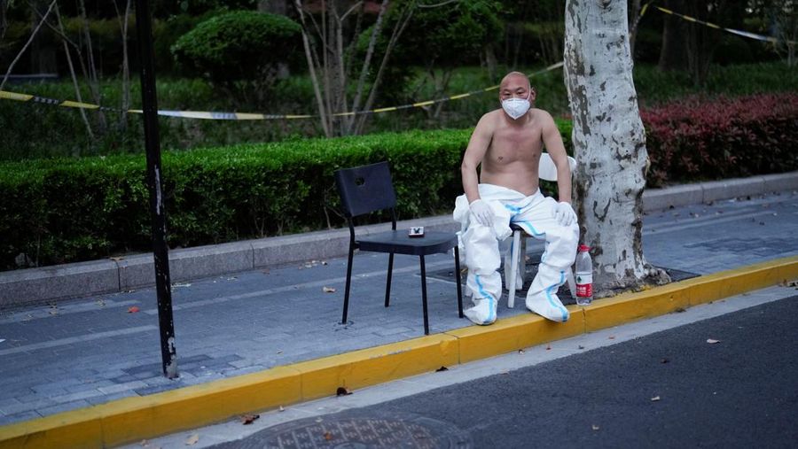 Seseorang dengan pakaian pelindung meemanjat barikade yang dipasang di sekitar area tertutup, selama penguncian untuk mengekang penyebaran penyakit coronavirus (COVID-19) di Shanghai, China, Senin (11/4/2022). (REUTERS/Aly Song)