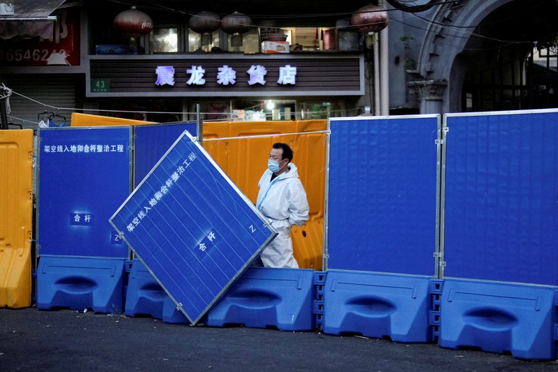 Seseorang dengan pakaian pelindung meemanjat barikade yang dipasang di sekitar area tertutup, selama penguncian untuk mengekang penyebaran penyakit coronavirus (COVID-19) di Shanghai, China, Senin (11/4/2022). (REUTERS/Aly Song)