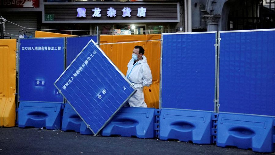 Seseorang dengan pakaian pelindung meemanjat barikade yang dipasang di sekitar area tertutup, selama penguncian untuk mengekang penyebaran penyakit coronavirus (COVID-19) di Shanghai, China, Senin (11/4/2022). (REUTERS/Aly Song)