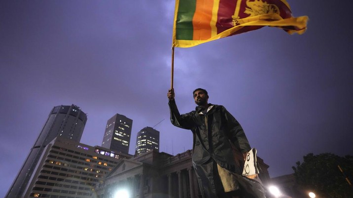 Seorang pria mengibarkan bendera nasional Sri Lanka saat dia berdiri di barikade yang menghalangi pintu masuk ke kantor presiden selama protes di Kolombo, Sri Lanka, Senin (11/4/2022). Ribuan warga Sri Lanka memprotes menyerukan agar presiden negara itu mengundurkan diri di tengah krisis ekonomi terburuk dalam sejarah. (AP Photo/Eranga Jayawardena)