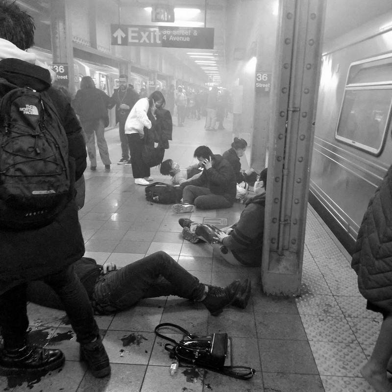 Penembakan di kereta bawah tanah di New York City, Amerika Serikat Penumpang membantu korban penembakan di luar gerbong kereta bawah tanah di wilayah Brooklyn di New York, Selasa (12/4/2022). Sejumlah penumpang diberondong tembakan pria tak dikenal di kereta bawah tanah di New York City saat jam sibuk pagi hari yang menyebabkan penumpang terluka berdarah di peron kereta. (Will B Wylde via AP)