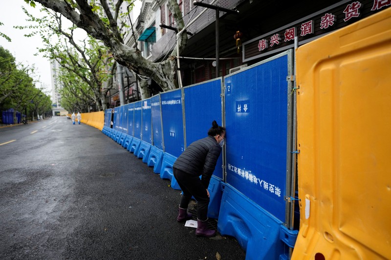 Seorang warga terlihat di balik pembatas yang menutup area yang dikunci di tengah pandemi penyakit virus corona (COVID-19), di Shanghai, China, Kamis (14/4/2022). (REUTERS/Aly Song)