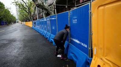 Seorang wanita membeli makanan dari penjual di belakang barikade area tertutup, selama penguncian di tengah pandemi penyakit coronavirus (COVID-19), di Shanghai, China, Kamis (14/4/2022). (REUTERS/Aly Song)