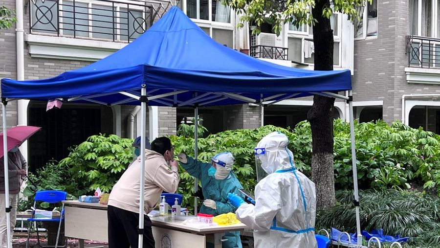 Seorang pekerja medis dengan pakaian pelindung melakukan pemeriskaan Covid-19 dari seorang penduduk di tempat pengujian aswab darurat di dalam kompleks perumahan yang dikunci, di tengah wabah penyakit coronavirus (COVID-19) di Shanghai, China, Kamis (14/4/2022). (REUTERS/Xihao Jiang)