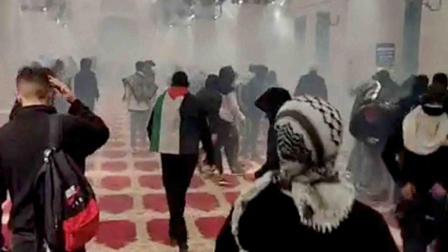 A worshiper wears a Palestinian flag, as smoke is seen inside the al-Aqsa mosque known to Muslims as the Noble Sanctuary and to Jews as the Temple Mount, during clashes with Israeli security forces, in Jerusalem's Old City, April 15, 2022 in this still image obtained from a social media video. Mujahed Hamayel/via REUTERS  THIS IMAGE HAS BEEN SUPPLIED BY A THIRD PARTY. MANDATORY CREDIT. NO RESALES. NO ARCHIVES.