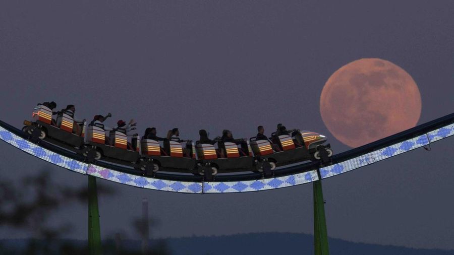 The moon rises behind the Alpina Bahn at Frankfurt's Dippemess, a traditional German fair, Saturday, April 16, 2022. (Sebastian Gollnow/dpa via AP)