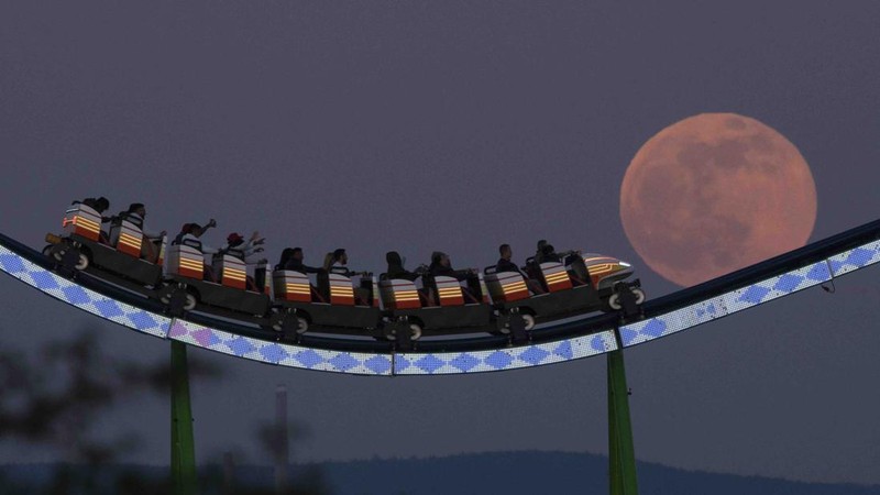 The moon rises behind the Alpina Bahn at Frankfurt's Dippemess, a traditional German fair, Saturday, April 16, 2022. (Sebastian Gollnow/dpa via AP)