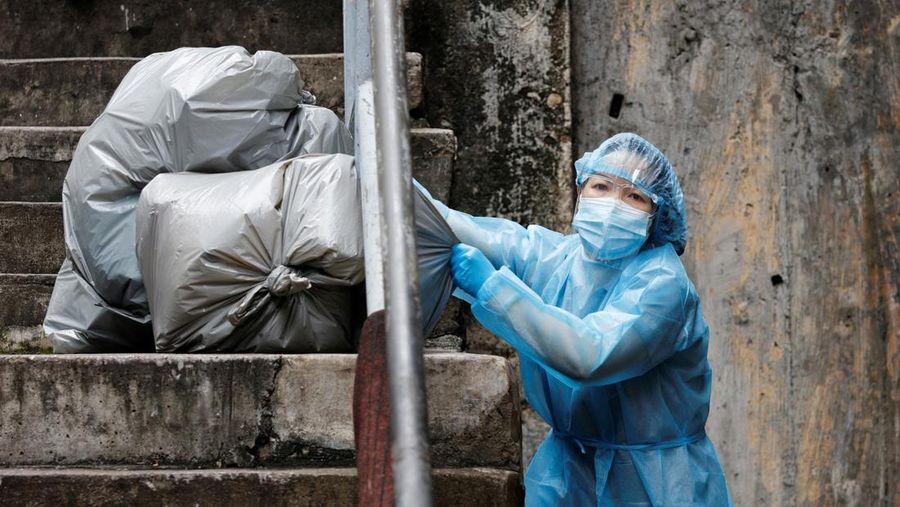 A cleaner wearing personal protective equipment (PPE) dumps garbage outside a quarantine hotel during the coronavirus disease (COVID-19) pandemic, in Hong Kong, China, April 2, 2022. Picture taken April 2, 2022. REUTERS/Tyrone Siu