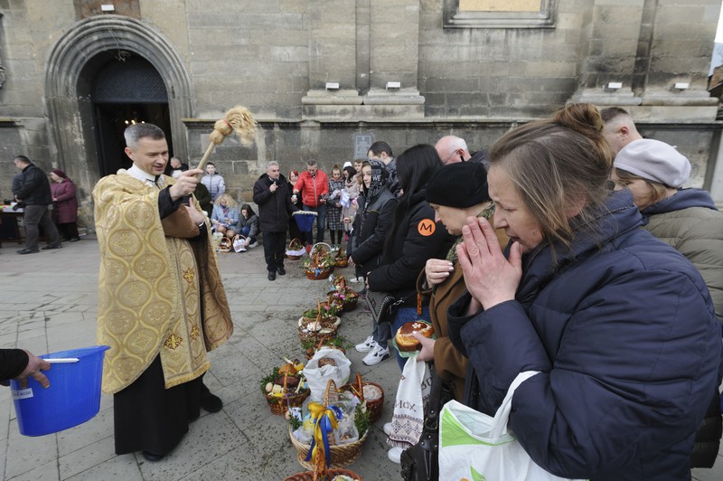 Seorang pastor Ukraina memberkati umat beriman saat mereka mengumpulkan kue tradisional dan telur yang dicat yang disiapkan untuk perayaan Paskah di Lviv, Ukraina, Sabtu (23/2/2022). (AP Photo/Mykola Tys)