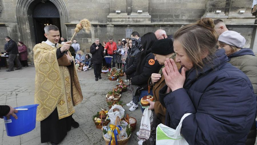Seorang pastor Ukraina memberkati umat beriman saat mereka mengumpulkan kue tradisional dan telur yang dicat yang disiapkan untuk perayaan Paskah di Lviv, Ukraina, Sabtu (23/2/2022). (AP Photo/Mykola Tys)