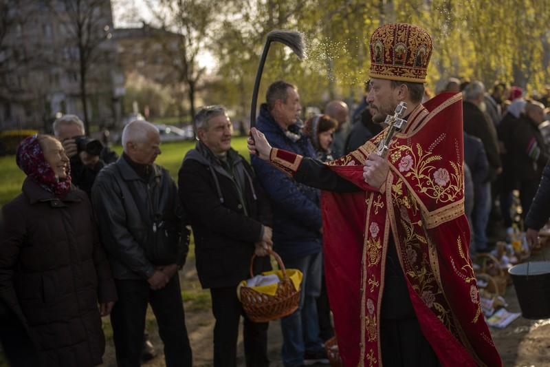 Seorang pastor Ukraina memberkati umat beriman saat mereka mengumpulkan kue tradisional dan telur yang dicat yang disiapkan untuk perayaan Paskah di Lviv, Ukraina, Sabtu (23/2/2022). (AP Photo/Mykola Tys)