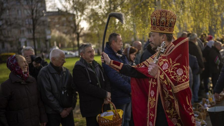 Seorang pastor Ukraina memberkati umat beriman saat mereka mengumpulkan kue tradisional dan telur yang dicat yang disiapkan untuk perayaan Paskah di Lviv, Ukraina, Sabtu (23/2/2022). (AP Photo/Mykola Tys)