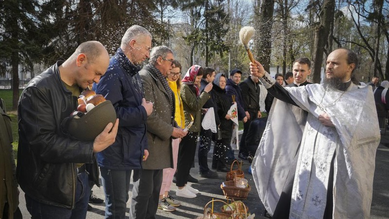 Seorang pastor Ukraina memberkati umat beriman saat mereka mengumpulkan kue tradisional dan telur yang dicat yang disiapkan untuk perayaan Paskah di Lviv, Ukraina, Sabtu (23/2/2022). (AP Photo/Mykola Tys)