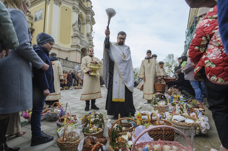 Seorang pastor Ukraina memberkati umat beriman saat mereka mengumpulkan kue tradisional dan telur yang dicat yang disiapkan untuk perayaan Paskah di Lviv, Ukraina, Sabtu (23/2/2022). (AP Photo/Mykola Tys)
