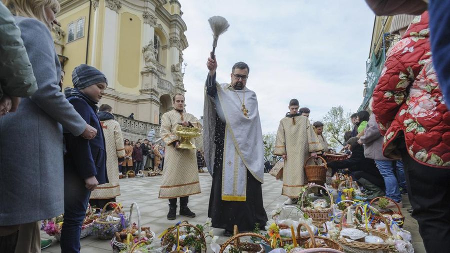 Seorang pastor Ukraina memberkati umat beriman saat mereka mengumpulkan kue tradisional dan telur yang dicat yang disiapkan untuk perayaan Paskah di Lviv, Ukraina, Sabtu (23/2/2022). (AP Photo/Mykola Tys)