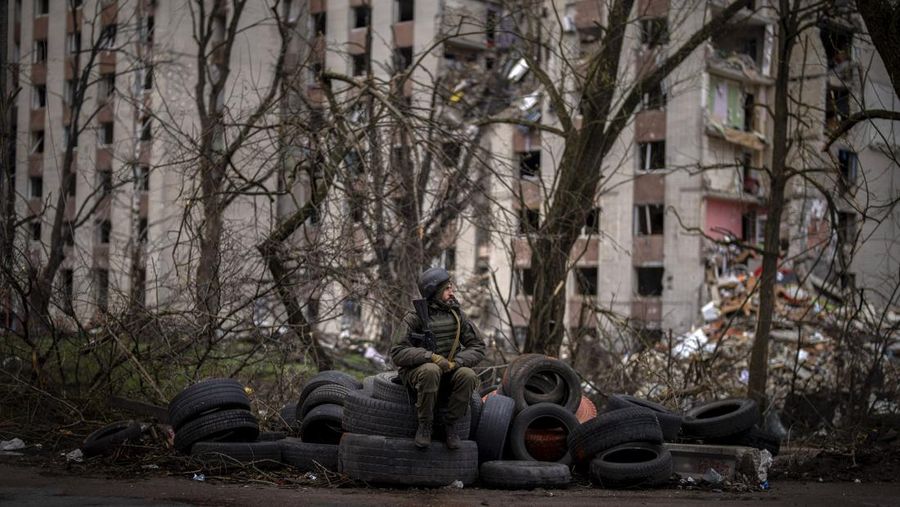 Seorang tentara Ukraina duduk di atas ban di samping gedung yang hancur akibat bom Rusia di Chernihiv, Ukraina, Sabtu (23/4/2022). (AP Photo/Emilio Morenatti)