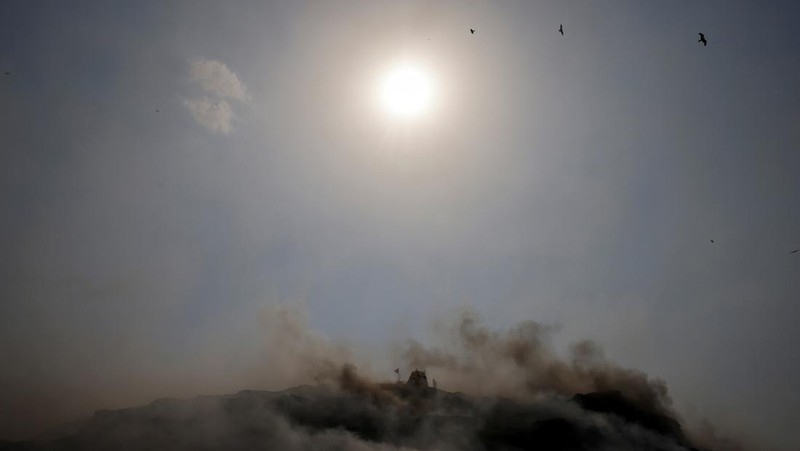 An excavator tries to contain the fire as smoke billows from burning garbage on a hot summer day, at the Bhalswa landfill site in New Delhi, India, April 29, 2022. REUTERS/Adnan Abidi     TPX IMAGES OF THE DAY