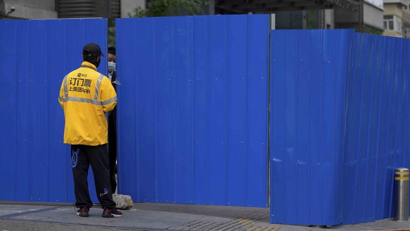 A resident wearing a face mask stands watch behind a barricaded fence of a locked-down residential complex on Thursday, April 28, 2022, in Beijing. China employs a variety of metal barricades, metal sheeting and door locks to keep people inside their apartments, buildings or complexes during lockdowns. The barriers have been deployed in multiple cities across China as part of the fight against COVID-19. (AP Photo/Andy Wong)