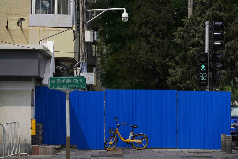 A resident wearing a face mask stands watch behind a barricaded fence of a locked-down residential complex on Thursday, April 28, 2022, in Beijing. China employs a variety of metal barricades, metal sheeting and door locks to keep people inside their apartments, buildings or complexes during lockdowns. The barriers have been deployed in multiple cities across China as part of the fight against COVID-19. (AP Photo/Andy Wong)