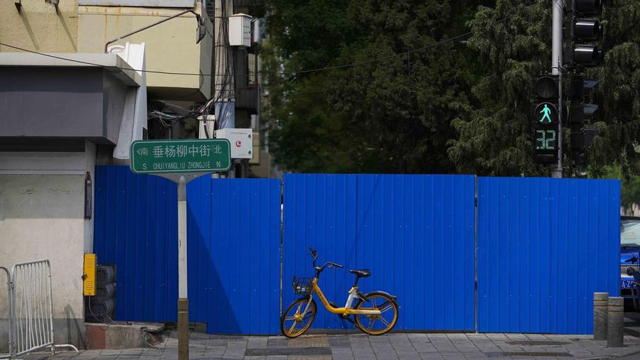 A resident wearing a face mask stands watch behind a barricaded fence of a locked-down residential complex on Thursday, April 28, 2022, in Beijing. China employs a variety of metal barricades, metal sheeting and door locks to keep people inside their apartments, buildings or complexes during lockdowns. The barriers have been deployed in multiple cities across China as part of the fight against COVID-19. (AP Photo/Andy Wong)
