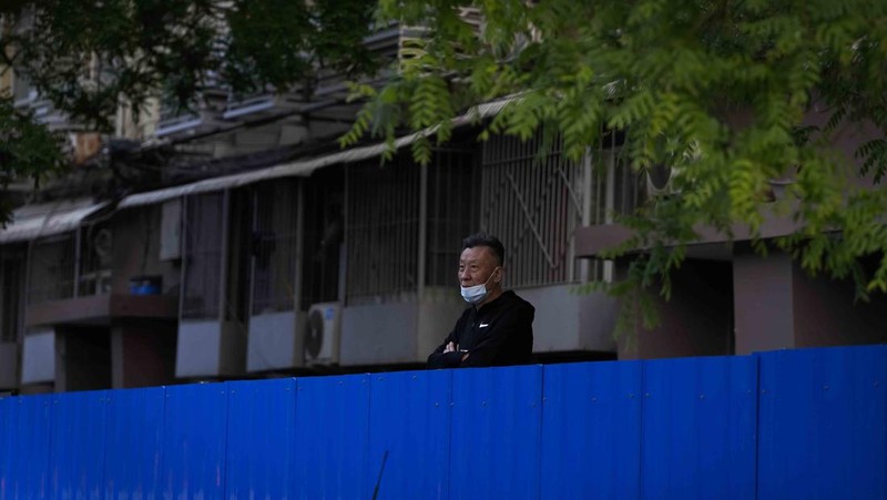 A resident wearing a face mask stands watch behind a barricaded fence of a locked-down residential complex on Thursday, April 28, 2022, in Beijing. China employs a variety of metal barricades, metal sheeting and door locks to keep people inside their apartments, buildings or complexes during lockdowns. The barriers have been deployed in multiple cities across China as part of the fight against COVID-19. (AP Photo/Andy Wong)