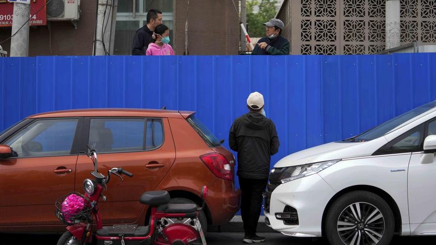 A resident wearing a face mask stands watch behind a barricaded fence of a locked-down residential complex on Thursday, April 28, 2022, in Beijing. China employs a variety of metal barricades, metal sheeting and door locks to keep people inside their apartments, buildings or complexes during lockdowns. The barriers have been deployed in multiple cities across China as part of the fight against COVID-19. (AP Photo/Andy Wong)
