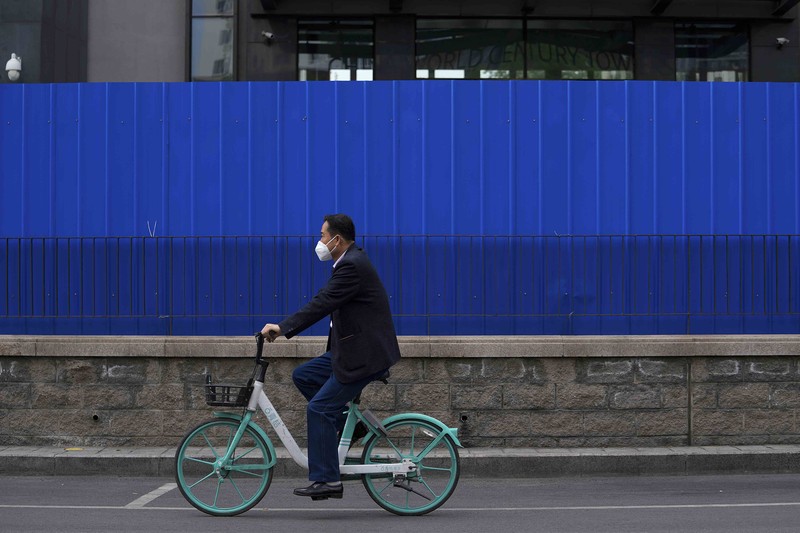 A resident wearing a face mask stands watch behind a barricaded fence of a locked-down residential complex on Thursday, April 28, 2022, in Beijing. China employs a variety of metal barricades, metal sheeting and door locks to keep people inside their apartments, buildings or complexes during lockdowns. The barriers have been deployed in multiple cities across China as part of the fight against COVID-19. (AP Photo/Andy Wong)