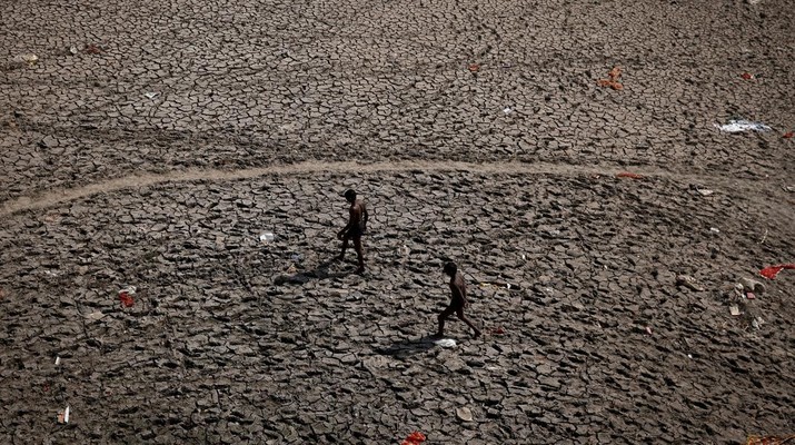 Pria berjalan melalui dasar sungai Yamuna yang hampir kering setelah mencari bahan daur ulang pada hari musim panas di New Delhi, India, Sabtu (30/4/2022). (REUTERS/Adnan Abidi)