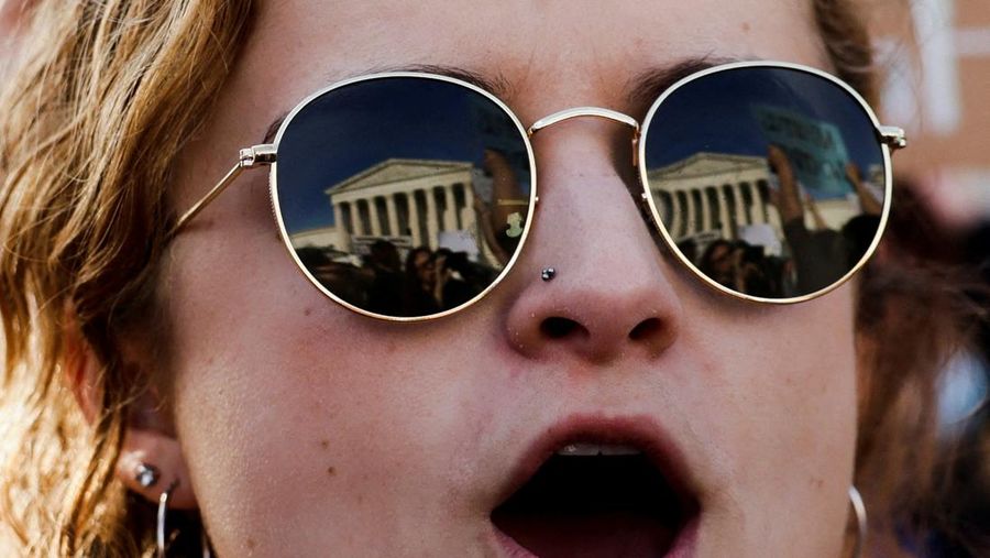 Refleksi Mahkamah Agung AS pada kacamata Hannah Fuller (25) selama protes setelah bocornya draf pendapat mayoritas yang ditulis oleh Hakim Samuel Alito mempersiapkan mayoritas pengadilan untuk membatalkan keputusan hak aborsi penting Roe v. Wade nanti tahun ini, di Washington, AS, Selasa (3/5/2022). (REUTERS/Evelyn Hockstein)
