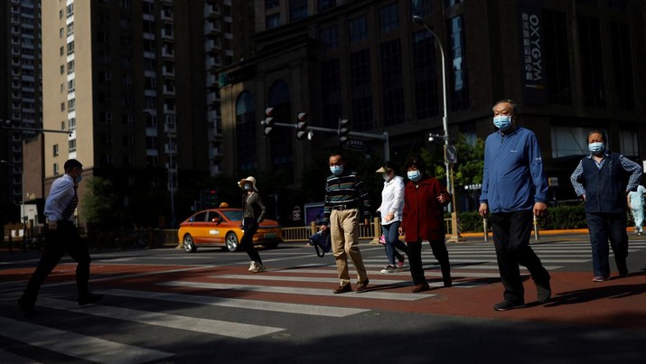 Orang-orang dengan menggunakani masker menyeberang jalan pada jam sibuk pagi hari di Central Business District (CBD) di distrik Chaoyang, di tengah wabah penyakit virus corona (COVID-19) di Beijing, China, Kamis (5/4/2022). (REUTERS/Carlos Garcia Rawlins)