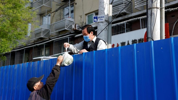 Penguncian Lockdown Covid-19 di Beijing China Seorang pria menerima sekantong sayuran sambil berdiri di belakang penghalang yang menutup kompleks perumahan saat diterapkan penguncian untuk menekan penyebaran Covid-19 di Beijing, China, Kamis (28/4/2022). (REUTERS/Carlos Garcia Rawlins)