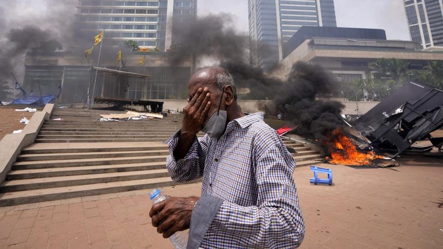 A Sri Lankan man reacts to tear gas as he walks past the vandalized site of anti-government protests outside president's office in Colombo, Sri Lanka, Monday, May 9, 2022. Authorities deployed armed troops in the capital Colombo on Monday hours after government supporters attacked protesters who have been camped outside the offices of the country's president and prime minster, as trade unions began a “Week of Protests” demanding the government change and its president to step down over the country’s worst economic crisis in memory. (AP Photo/Eranga Jayawardena)