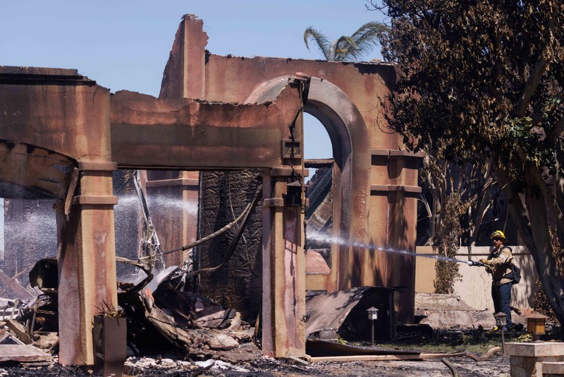 A firefighter sprays water on the remains of a burned-out home after a fast-moving wildfire ripped through an affluent neighborhood in Laguna Niguel, California, U.S., May 12, 2022. REUTERS/Mike Blake