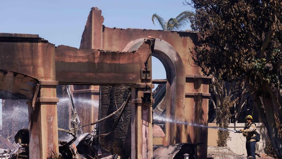A firefighter sprays water on the remains of a burned-out home after a fast-moving wildfire ripped through an affluent neighborhood in Laguna Niguel, California, U.S., May 12, 2022. REUTERS/Mike Blake