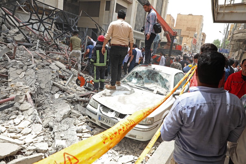 Warga Iran berkumpul di lokasi di mana sebuah bangunan sepuluh lantai runtuh di barat daya kota Abadan, Iran, Senin (23/5/2022).  Kejadian tersebut menyebabkan beberapa orang meninggal dan sekitar 80 orang terperangkap di bawah reruntuhan ketika sebuah bangunan yang belum selesai roboh di barat daya Iran. (Photo by -/TASNIM NEWS/AFP via Getty Images)