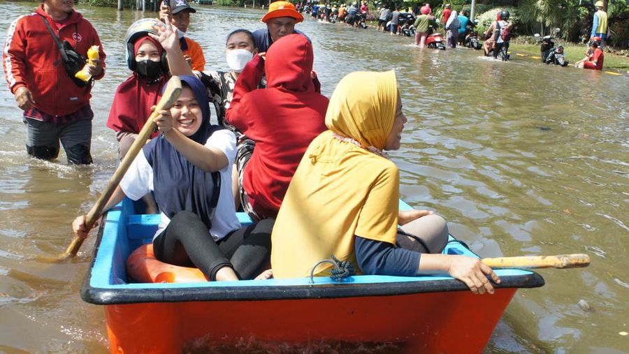 Para pekerja menggunakan perahu untuk meninggalkan pabrik mereka setelah gelombang pasang menghantam garis pantai utara yang melumpuhkan aktivitas pelabuhan di pelabuhan Tanjung Mas di Semarang, Jawa Tengah, Selasa (24/5/2022). (Photo by DAFFA RAMYA KANZUDDIN/AFP via Getty Images)