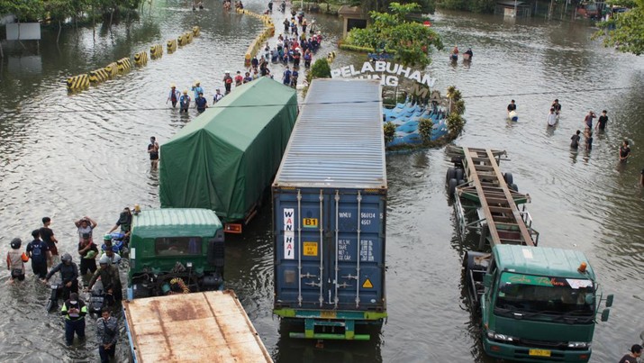 Pekerja melewati banjir akibat gelombang pasang menghantam garis pantai utara yang melumpuhkan aktivitas pelabuhan di pelabuhan Tanjung Mas di Semarang, Jawa Tengah, Selasa (24/5/2022). (Photo by DAFFA RAMYA KANZUDDIN/AFP via Getty Images)