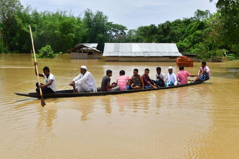 Anak-anak menaiki rakit bambu melewati daerah banjir setelah hujan lebat di distrik Morigaon, negara bagian Assam, India, Minggu (22/5/2022). Banjir adalah ancaman biasa bagi jutaan orang di dataran rendah Bangladesh dan tetangga timur laut India, tetapi banyak ahli mengatakan bahwa perubahan iklim meningkatkan frekuensi, keganasan dan ketidakpastian. (Photo by BIJU BORO/AFP via Getty Images)