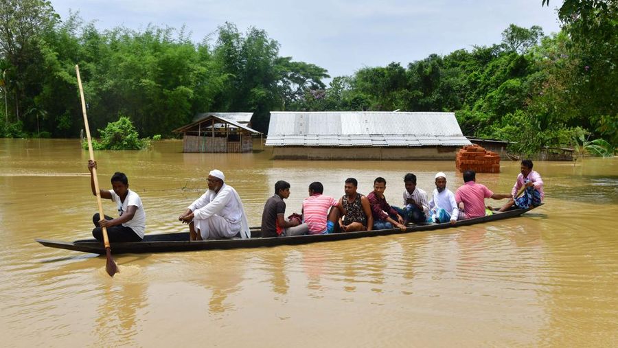 Anak-anak menaiki rakit bambu melewati daerah banjir setelah hujan lebat di distrik Morigaon, negara bagian Assam, India, Minggu (22/5/2022). Banjir adalah ancaman biasa bagi jutaan orang di dataran rendah Bangladesh dan tetangga timur laut India, tetapi banyak ahli mengatakan bahwa perubahan iklim meningkatkan frekuensi, keganasan dan ketidakpastian. (Photo by BIJU BORO/AFP via Getty Images)