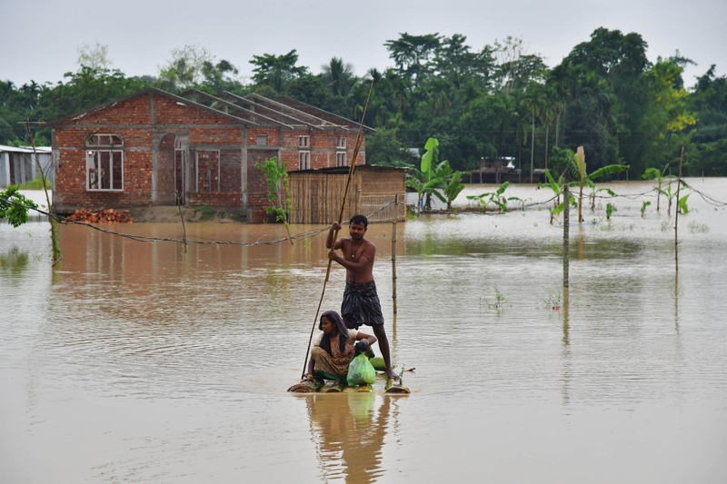 Anak-anak menaiki rakit bambu melewati daerah banjir setelah hujan lebat di distrik Morigaon, negara bagian Assam, India, Minggu (22/5/2022). Banjir adalah ancaman biasa bagi jutaan orang di dataran rendah Bangladesh dan tetangga timur laut India, tetapi banyak ahli mengatakan bahwa perubahan iklim meningkatkan frekuensi, keganasan dan ketidakpastian. (Photo by BIJU BORO/AFP via Getty Images)