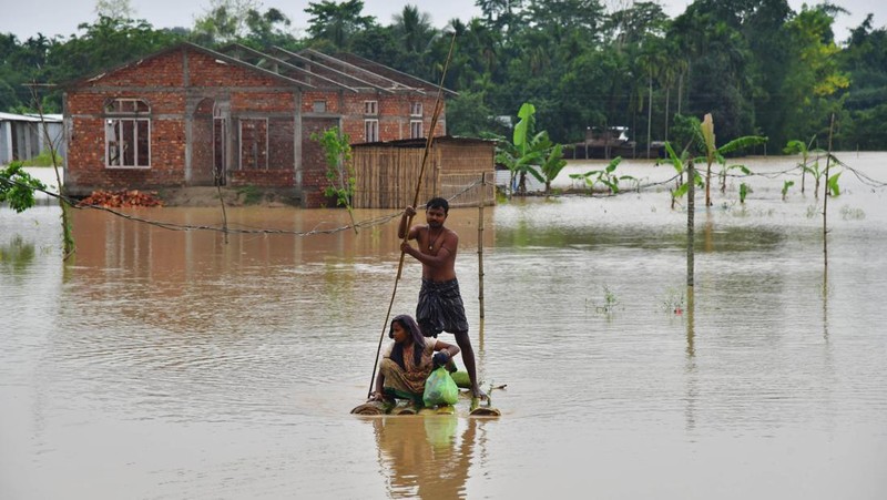 Anak-anak menaiki rakit bambu melewati daerah banjir setelah hujan lebat di distrik Morigaon, negara bagian Assam, India, Minggu (22/5/2022). Banjir adalah ancaman biasa bagi jutaan orang di dataran rendah Bangladesh dan tetangga timur laut India, tetapi banyak ahli mengatakan bahwa perubahan iklim meningkatkan frekuensi, keganasan dan ketidakpastian. (Photo by BIJU BORO/AFP via Getty Images)
