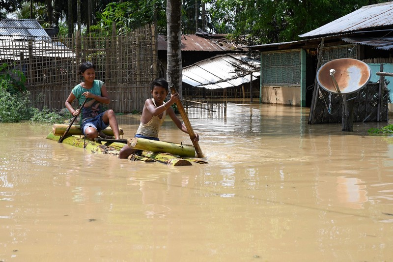 Anak-anak menaiki rakit bambu melewati daerah banjir setelah hujan lebat di distrik Morigaon, negara bagian Assam, India, Minggu (22/5/2022). Banjir adalah ancaman biasa bagi jutaan orang di dataran rendah Bangladesh dan tetangga timur laut India, tetapi banyak ahli mengatakan bahwa perubahan iklim meningkatkan frekuensi, keganasan dan ketidakpastian. (Photo by BIJU BORO/AFP via Getty Images)