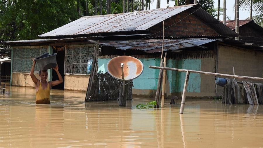 Anak-anak menaiki rakit bambu melewati daerah banjir setelah hujan lebat di distrik Morigaon, negara bagian Assam, India, Minggu (22/5/2022). Banjir adalah ancaman biasa bagi jutaan orang di dataran rendah Bangladesh dan tetangga timur laut India, tetapi banyak ahli mengatakan bahwa perubahan iklim meningkatkan frekuensi, keganasan dan ketidakpastian. (Photo by BIJU BORO/AFP via Getty Images)